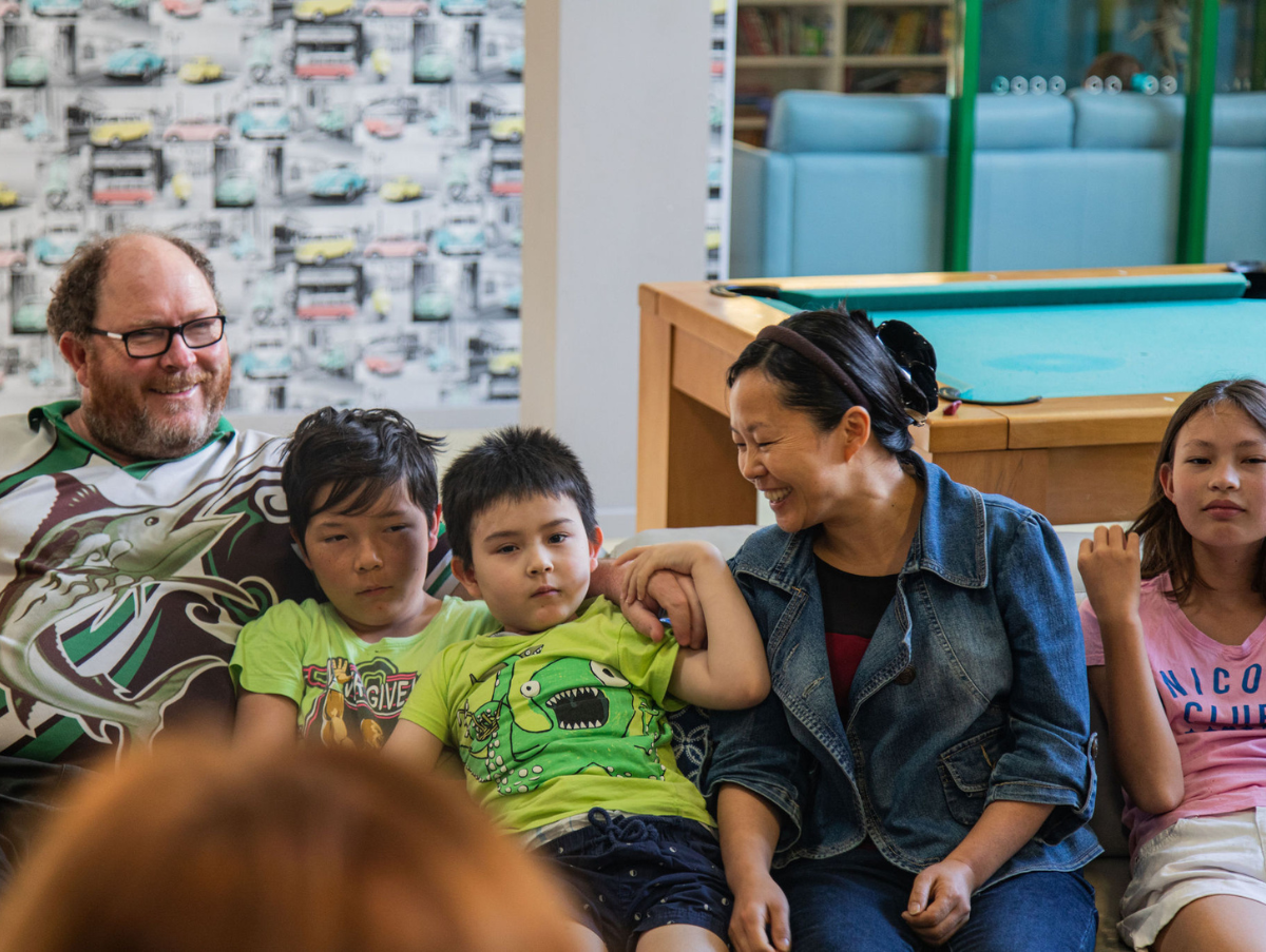 A mixed race family sitting on a lounge at the Ronald McDonald House Newcastle smiling and embracing each other